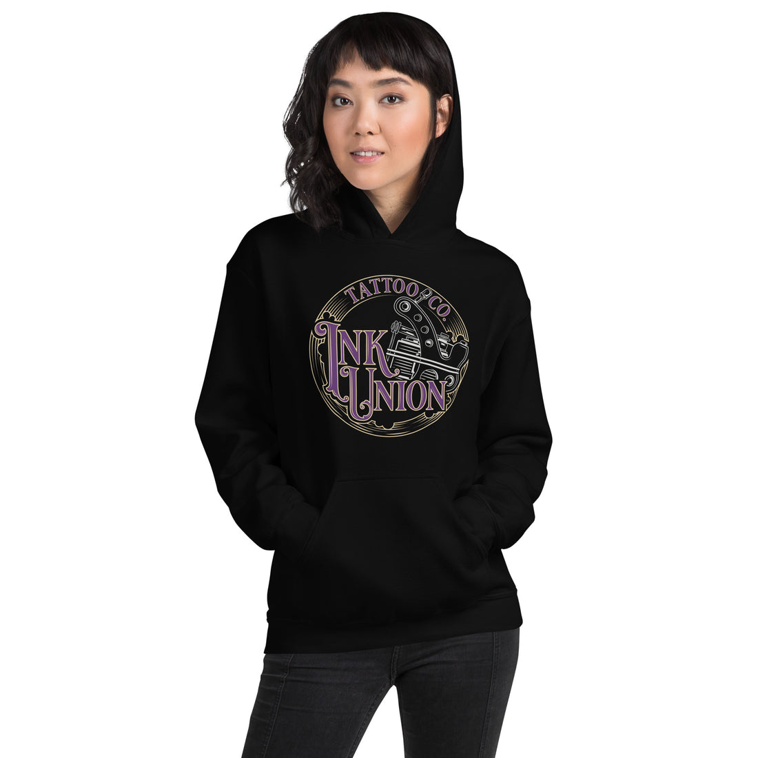 An attractive woman wearing a black hoodie  adorned with the Ink Union Tattoo Co.  purple and gold with a silver tattoo machine logo.