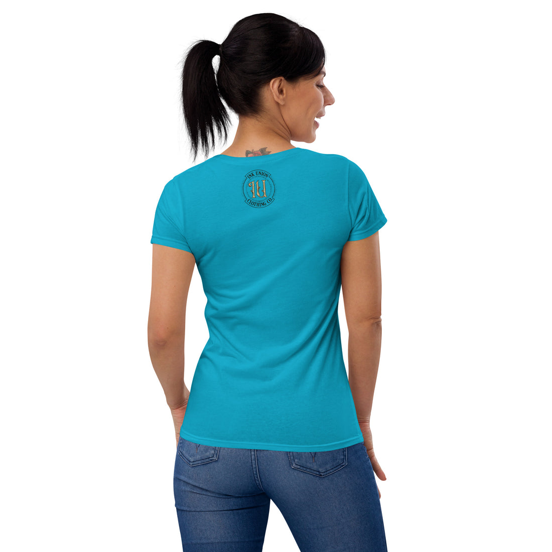 The back view of an attractive woman wearing a light blue t-shirt with a small gold and black Ink Union badge Logo centered just under the neckline.