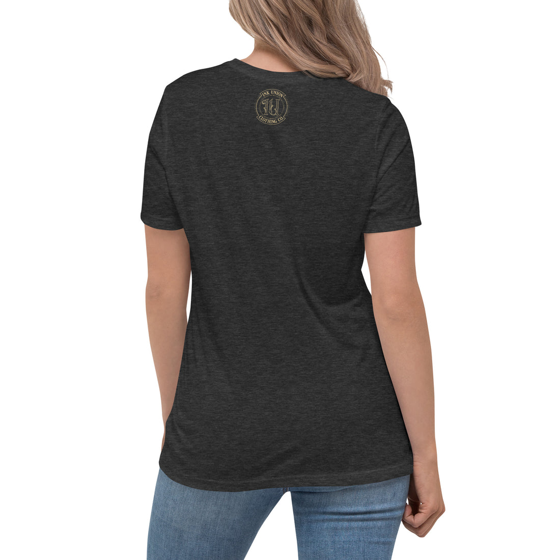 The back view of an attractive woman wearing a dark grey t-shirt with a small gold Ink Union Badge Logo centered just under the neckline.