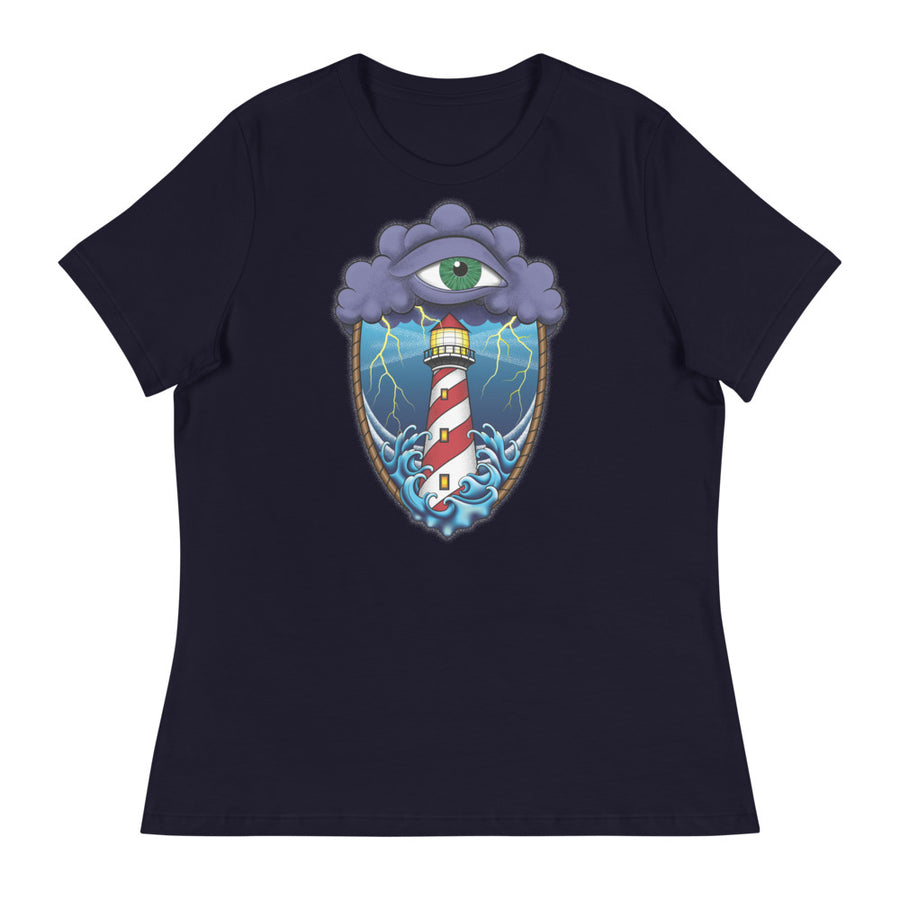 A navy blue t-shirt with an old school eye of the storm tattoo design of large dark purple storm clouds at the top of the design with a green eye in the middle of the clouds.  Below the clouds is an oval shape with brown rope. Inside the rope are stormy seas and lightning striking at a lighthouse that is white and red striped like a barber pole.